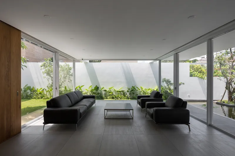Living room with floor-to-ceiling glazing overlooking planted courtyard garden under overcast sky