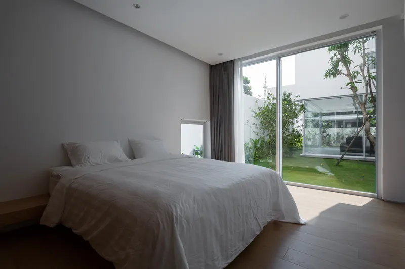 Bedroom interior with sliding glass wall overlooking an interior courtyard garden with lawn and trees