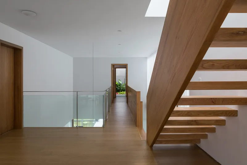 Upper level hallway with cantilevered timber staircase, glass guardrail, and skylights overhead