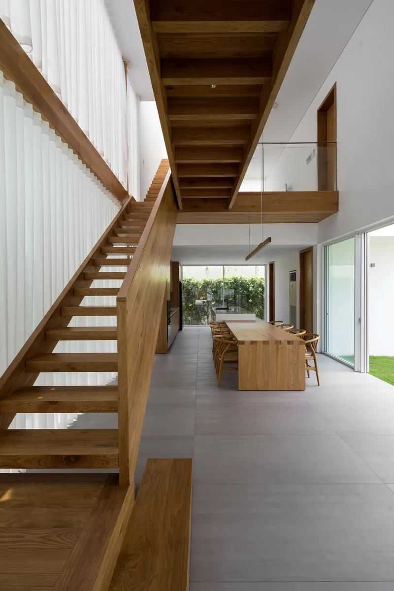 Open-tread timber staircase rising beside the dining area with glazed balustrade at the upper level