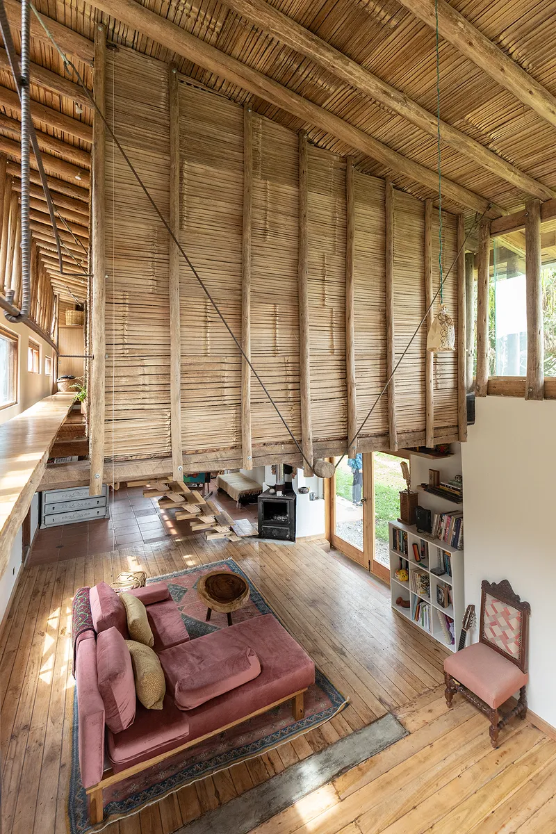 Living area with sloped bamboo ceiling, exposed timber beams, wooden flooring, and pink upholstered furniture