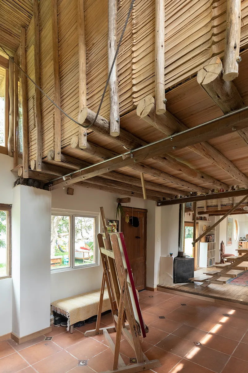 Interior corner showing a timber mezzanine platform, bamboo roof structure, and terracotta tile floor with sunlight