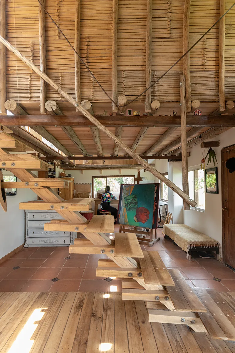 Open timber staircase beneath exposed beams and bamboo ceiling with a person working at the far end