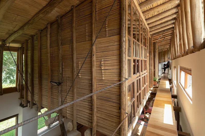 Narrow corridor with exposed bamboo slat ceiling and timber structural members alongside a white plastered wall