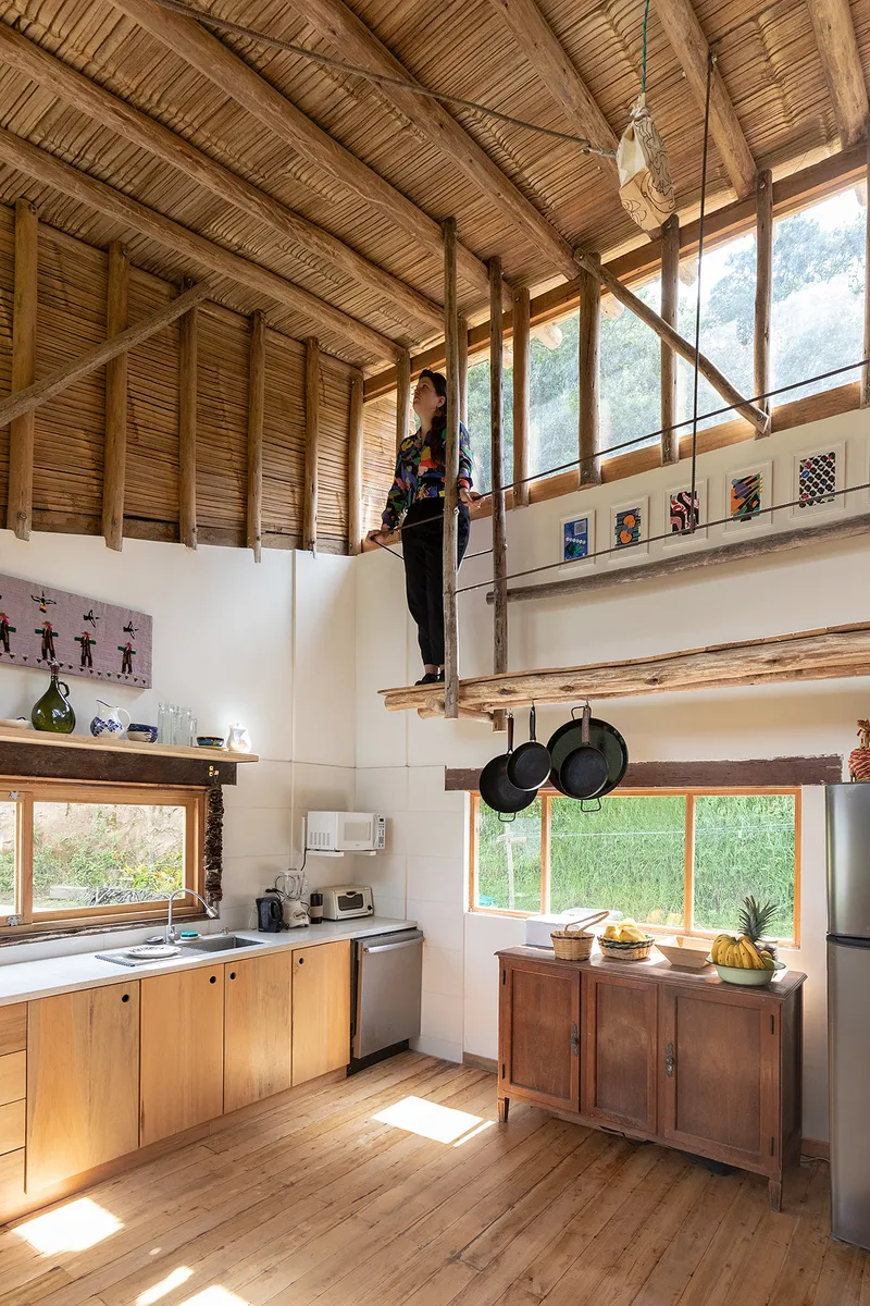 Double-height kitchen space with bamboo slat ceiling, timber beams, and a person standing on a mezzanine platform