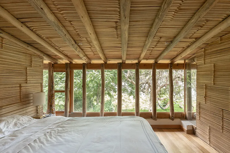Bedroom with bamboo slat ceiling and walls, floor-to-ceiling glazed doors opening to greenery beyond