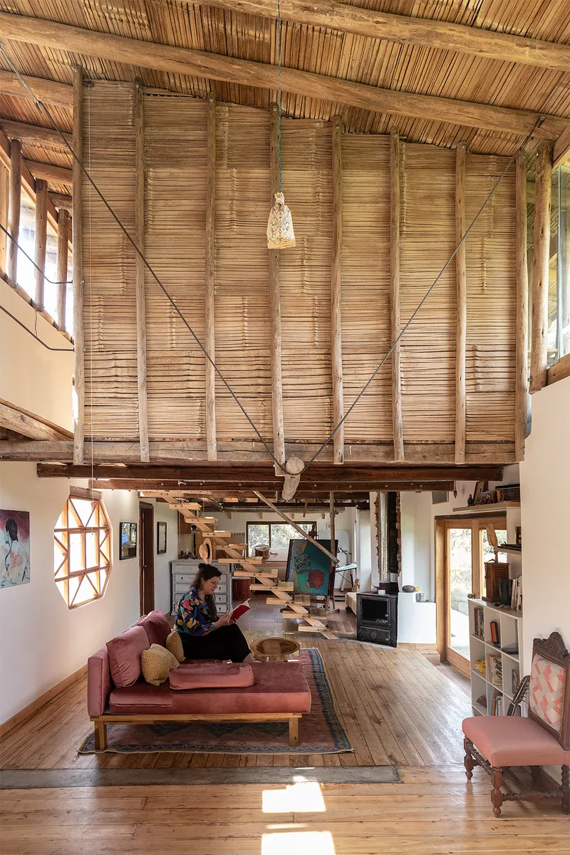 Double-height living room with mezzanine sleeping loft and person reading on pink sofa in afternoon light
