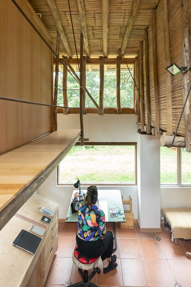 View from mezzanine workspace showing person at desk with horizontal window framing garden beyond