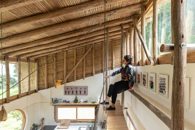 Person sitting on suspended timber walkway overlooking kitchen under bamboo-slat ceiling with diagonal bracing