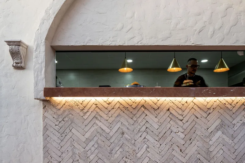 Service counter with herringbone brick base and backlit stone countertop beneath painted brick vault