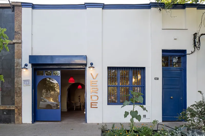 White stucco street facade with blue painted steel frames and arched doorway at twilight