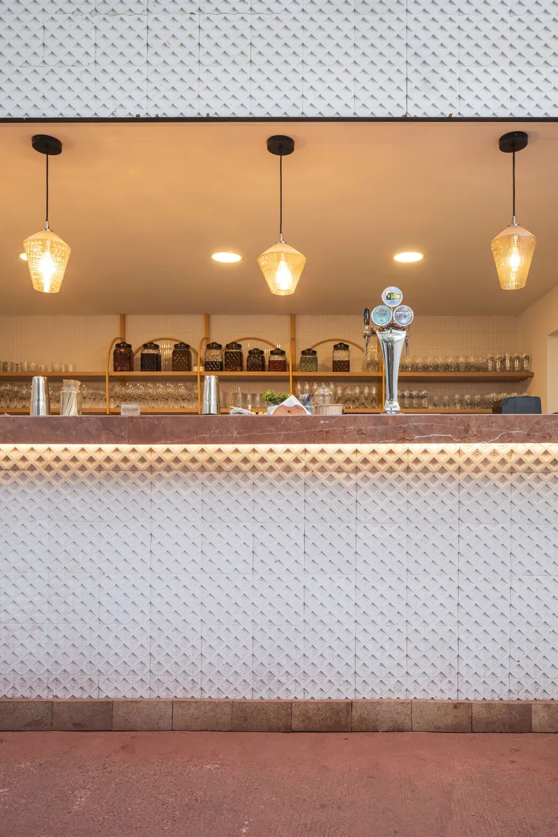 Bar counter with white diamond-patterned tile cladding and three amber pendant lights above