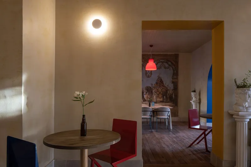 Interior view through a yellow-framed doorway connecting two dining spaces with circular wall sconces