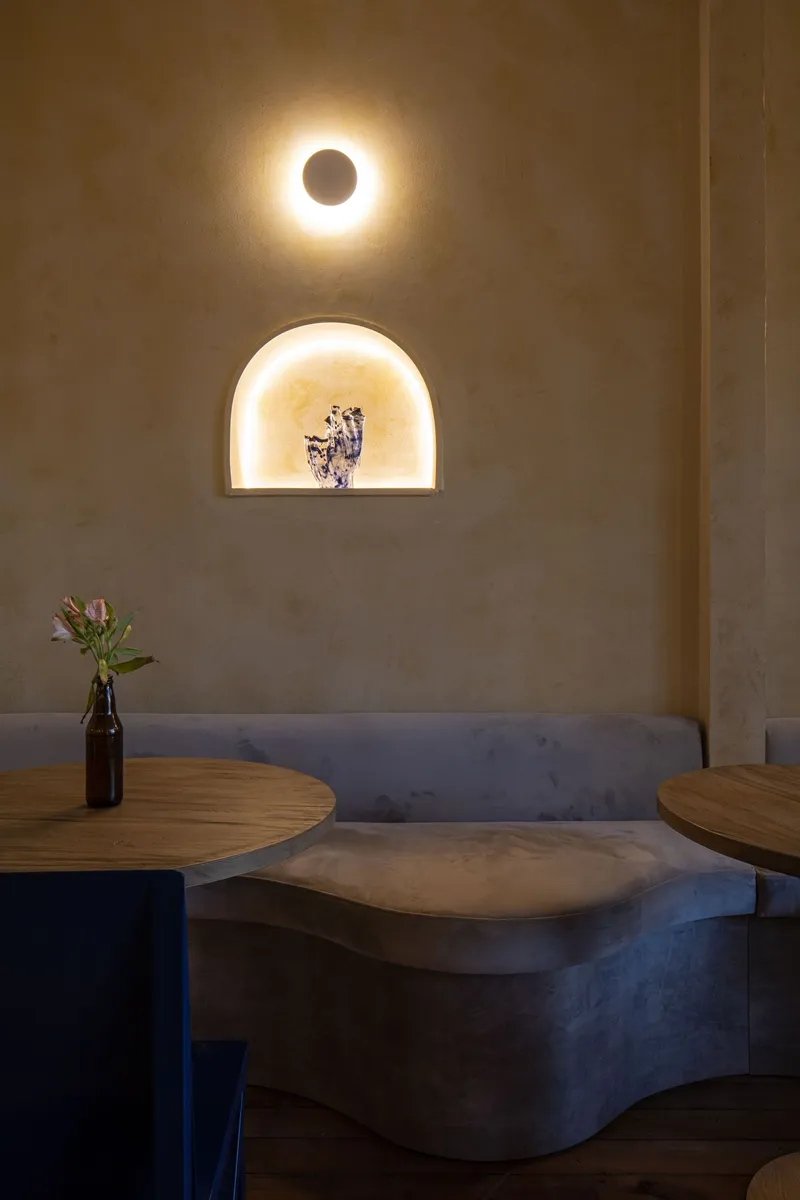 Corner banquette seating with curved concrete bench and arched wall niche lit from within