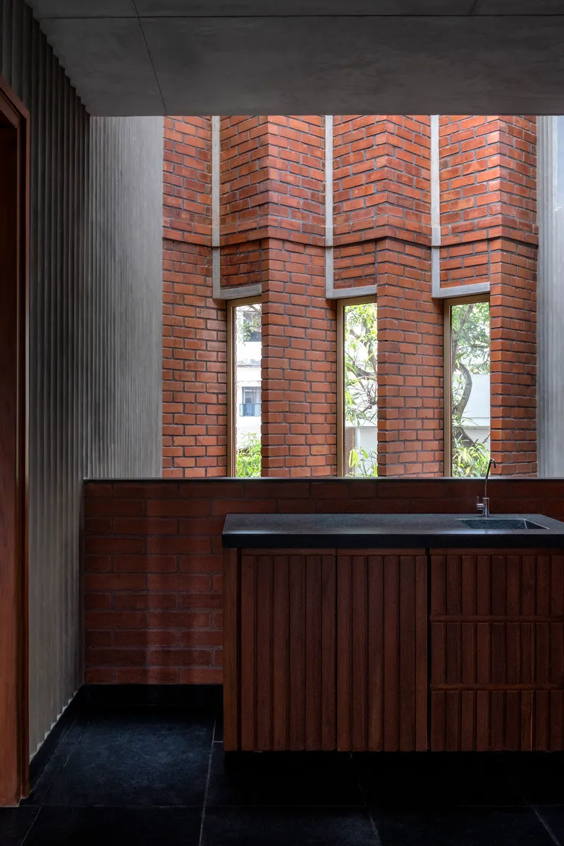 Bathroom vanity beneath herringbone patterned brick wall with vertical window slots framing greenery outside