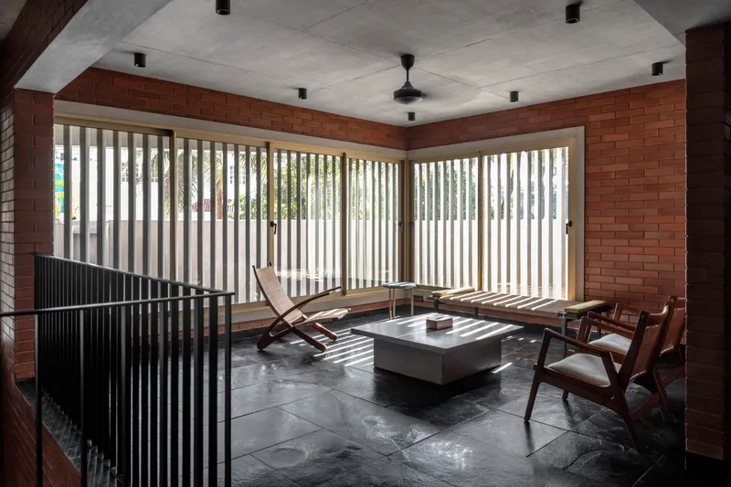 Living room with vertical timber louvres filtering daylight across brick walls and dark stone flooring