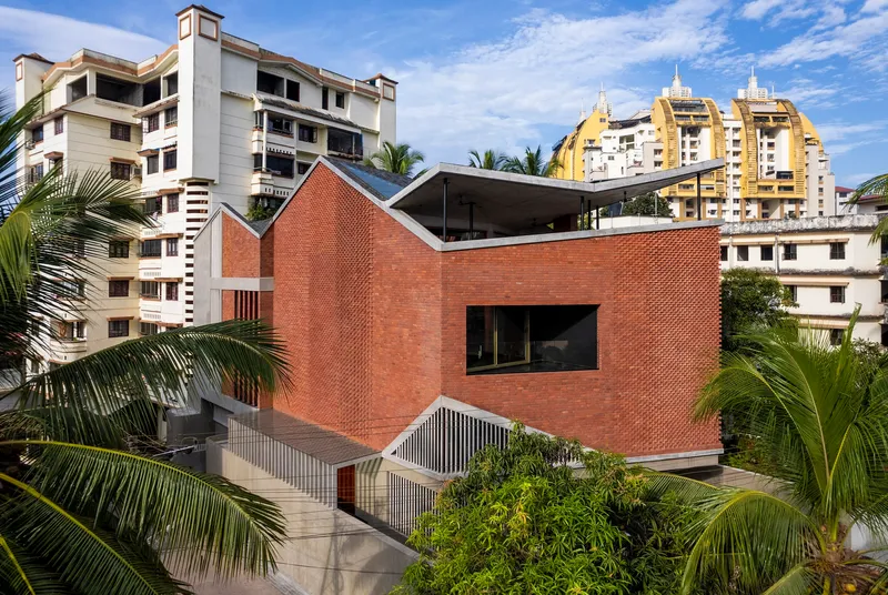 Elevated view of the red brick facade with perforated screens and folded roof amid palm trees and residential towers