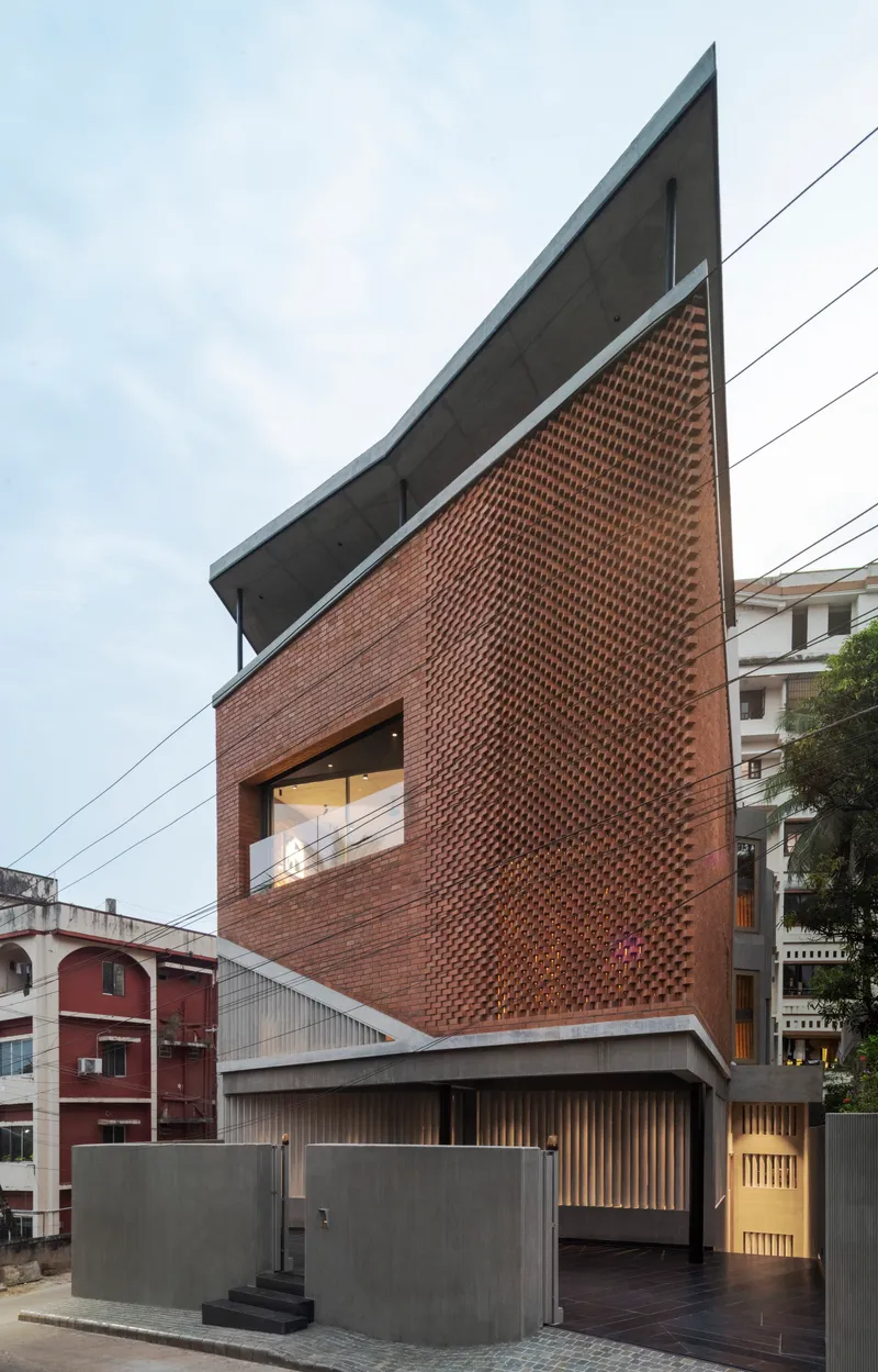Sharp angular facade with projecting brick screen and cantilevered concrete roof slab at dusk