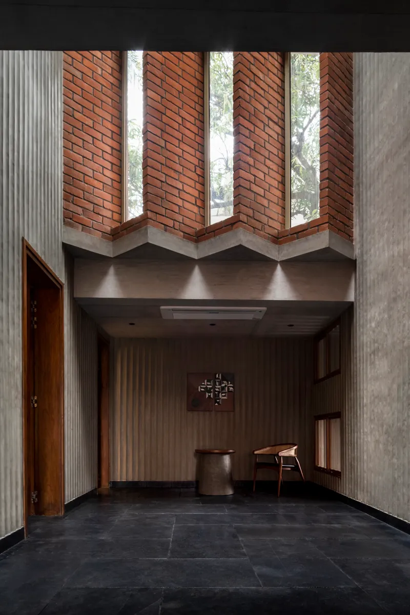 Double-height entry foyer with zigzag brick clerestory windows and concrete beams over dark stone flooring
