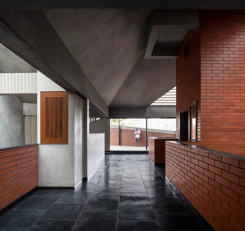 Interior corridor with exposed concrete ceiling and brick half-walls leading to a terrace with a figure walking