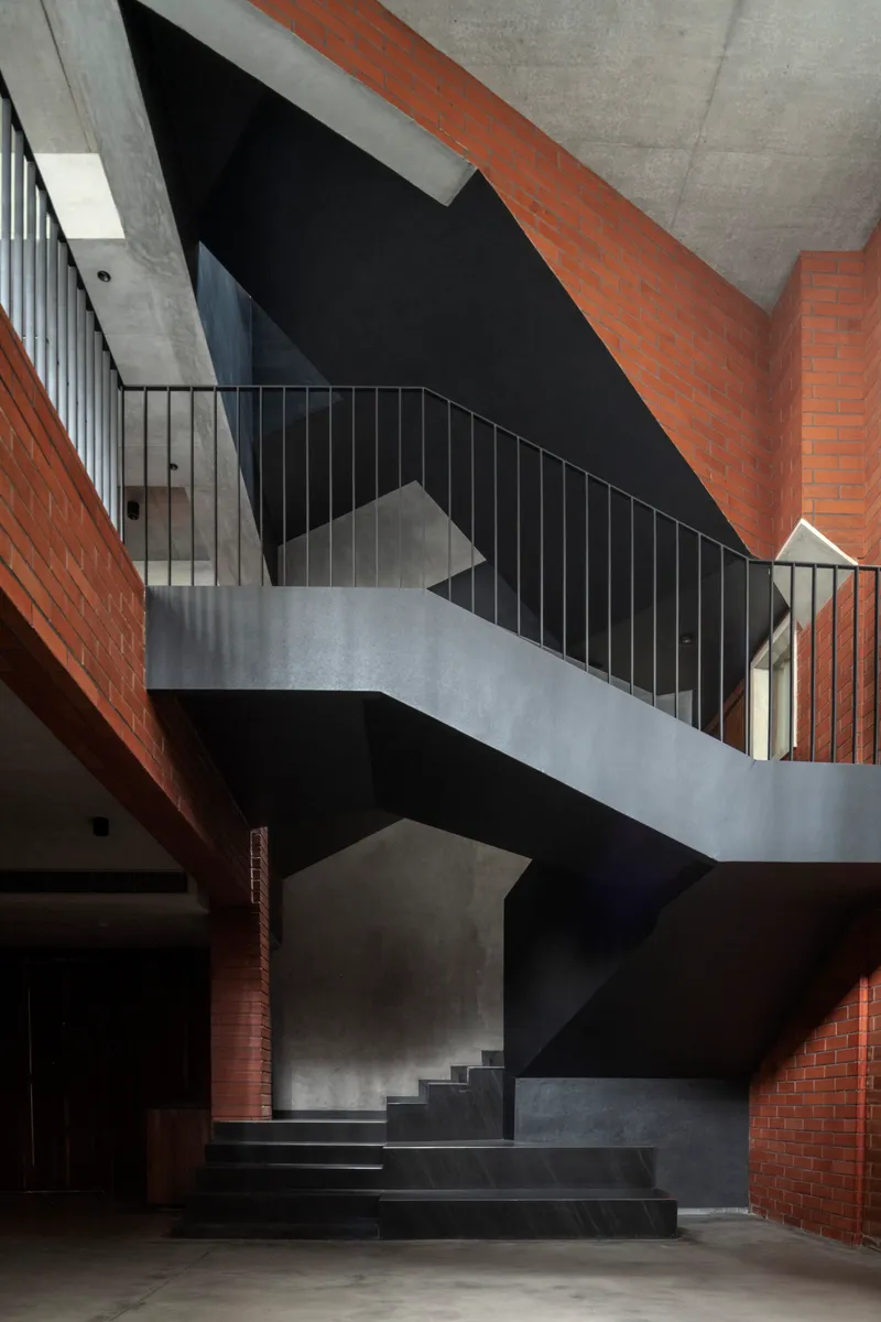 Vertical view of the folded concrete staircase with steel railings framed by red brick walls