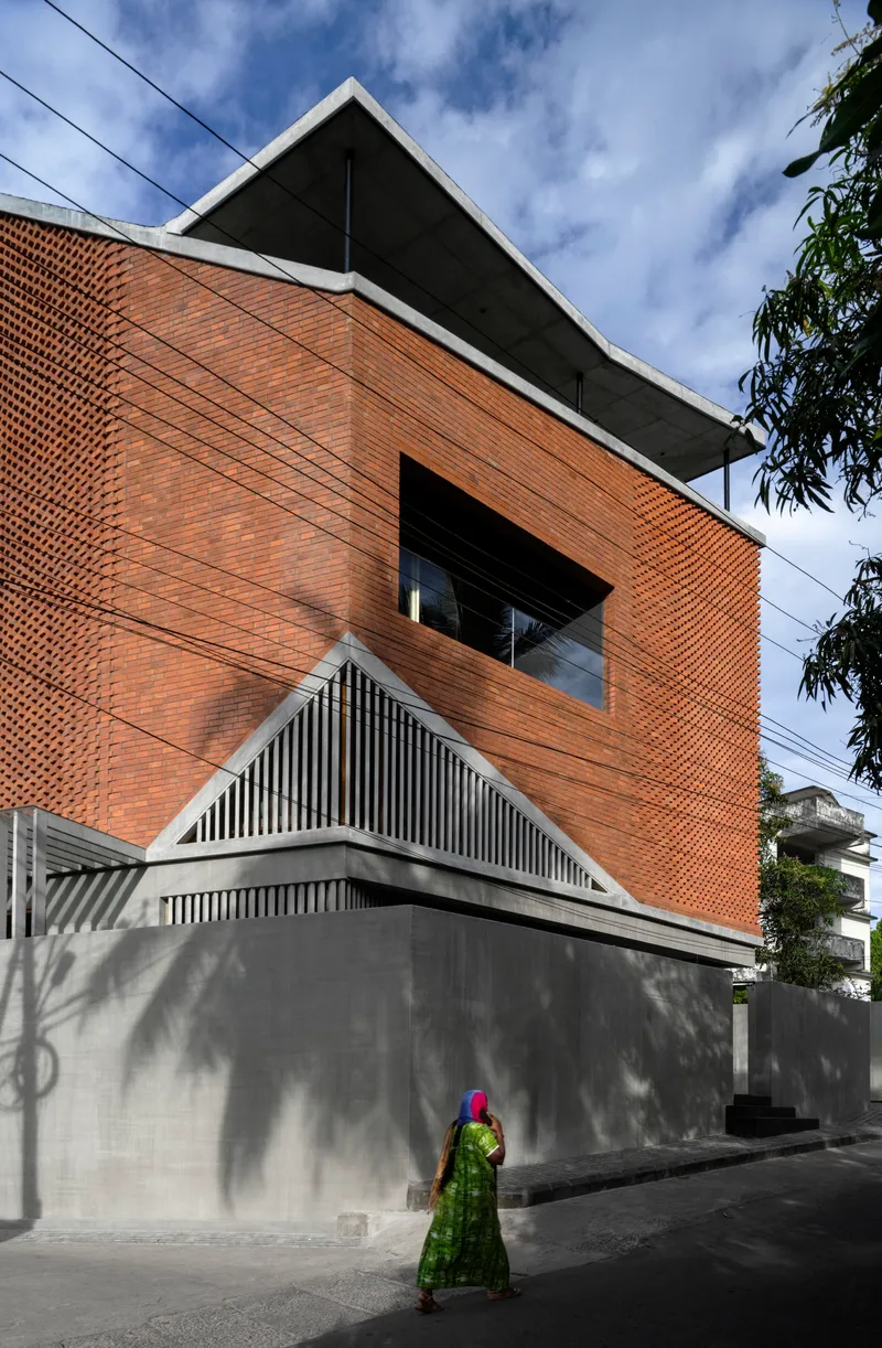 Street view of the brick lattice facade with a concrete base and a person in green walking below
