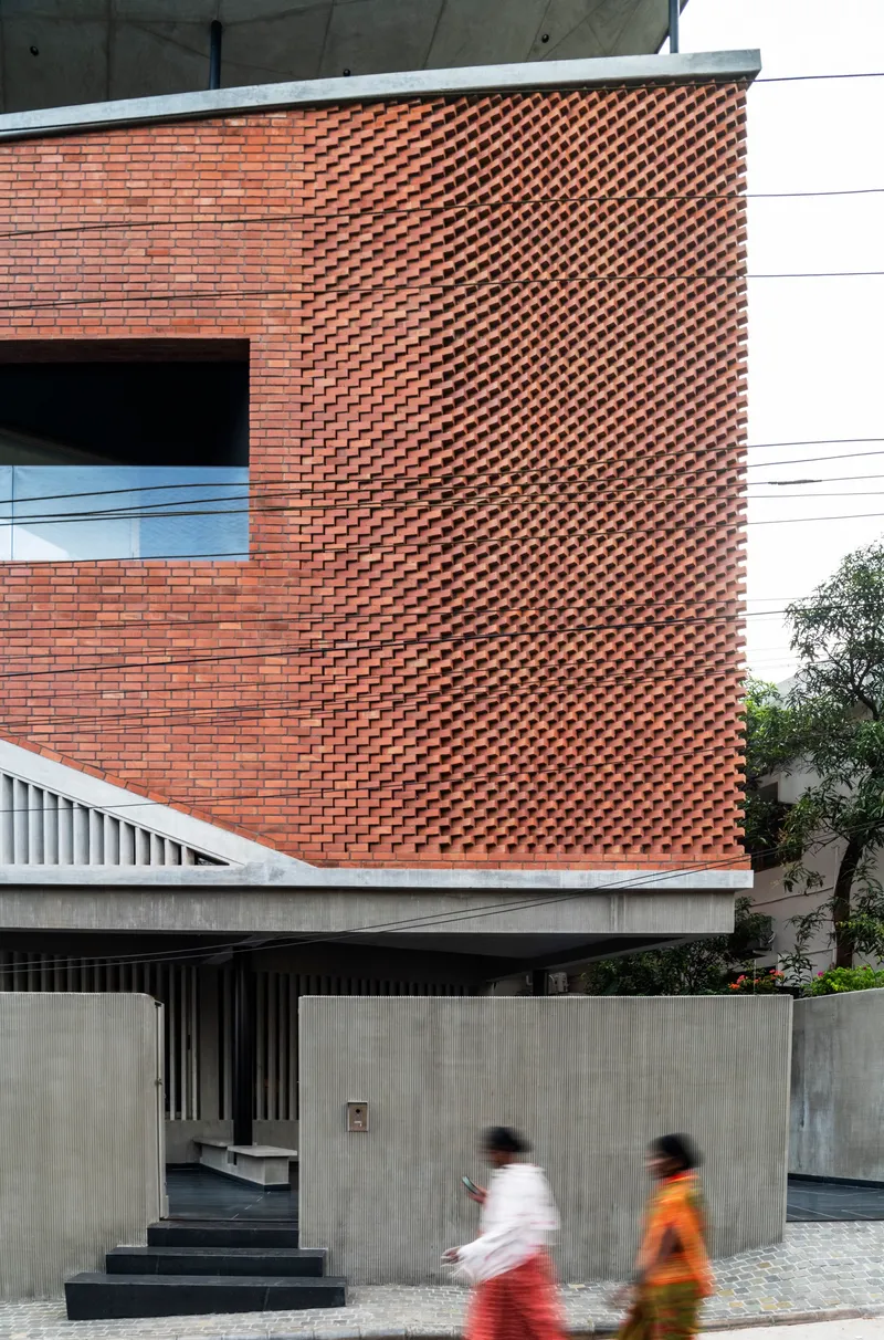 Textured brick facade above a concrete entrance with two figures in motion passing by