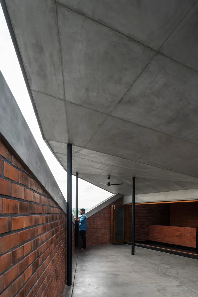 Covered terrace with exposed concrete ceiling, black steel columns, and red brick walls as a person stands in the passage