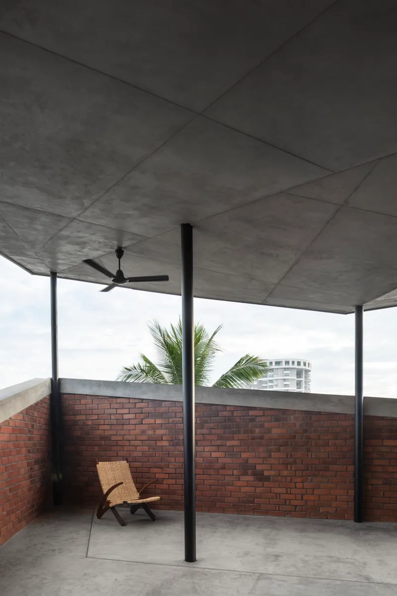 Rooftop terrace with concrete soffit, ceiling fan, steel columns, and brick parapet walls with palm fronds visible beyond