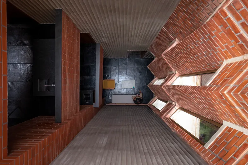 Interior corridor with zigzagging brick walls, clerestory windows, corrugated metal ceiling, and dark tile accent wall