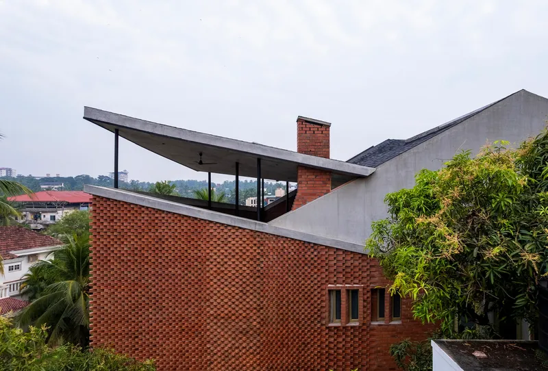 Exterior view showing cantilevered concrete roof planes above chequered brick facade and surrounding vegetation under overcast sky