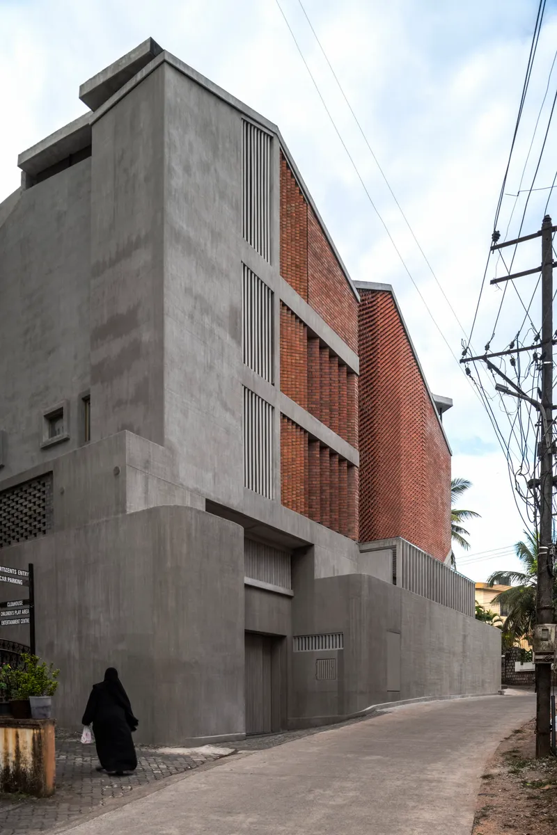 Street view of concrete and brick facade with vertical louvres and overhead power lines as a figure walks past