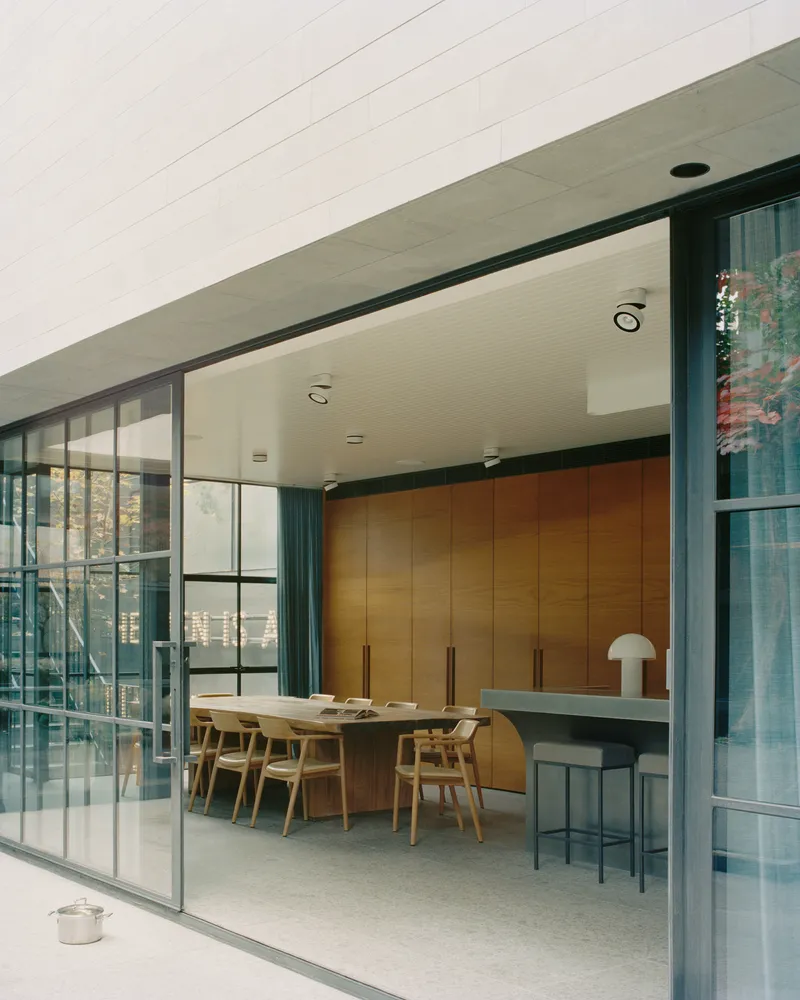 Sliding steel-framed glass doors opening onto a dining area with timber cabinetry and breakfast bar
