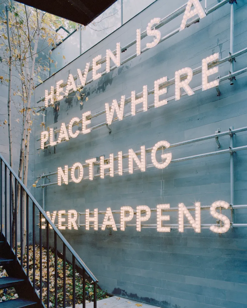 Glass-clad facade with text installation beside planted courtyard in dappled light