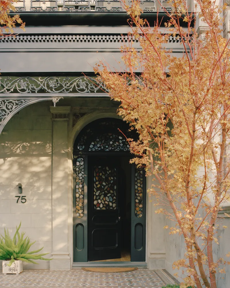 Entry porch with ornamental ironwork and glass door framed by autumn foliage