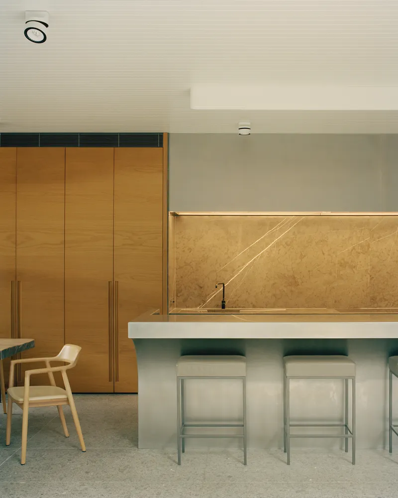 Kitchen island with pale counter and bar stools facing a bronze backsplash wall with oak cabinetry