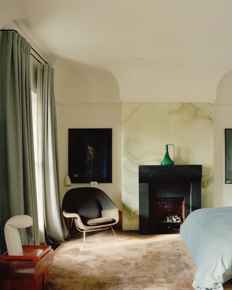 Bedroom with black fireplace surround against veined marble panel beneath arched ceiling and green curtains