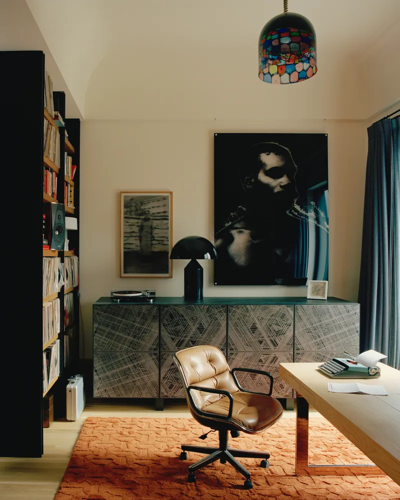Home office with patterned credenza beneath mosaic pendant light and tall bookshelves flanking the workspace