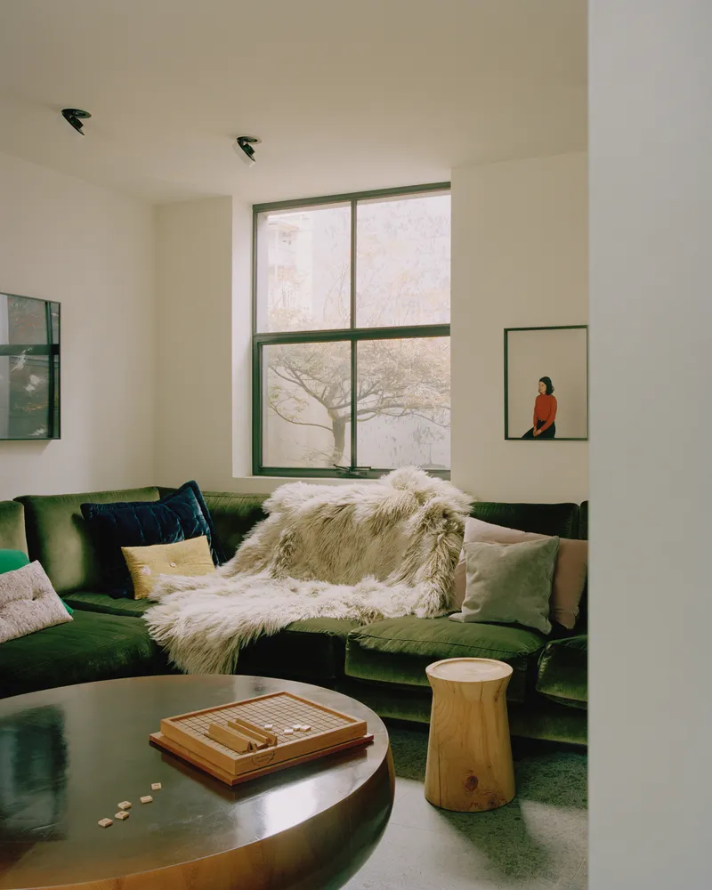 Living room with green velvet sofa and tall metal-framed window overlooking bare winter trees