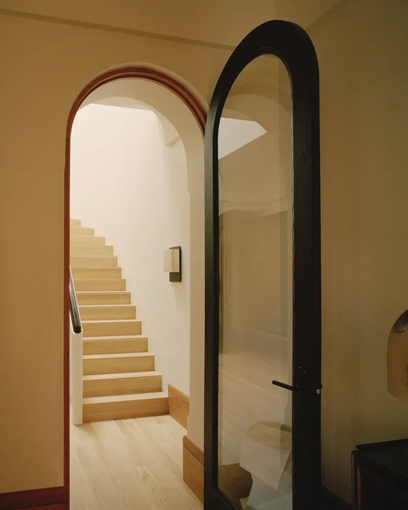 Arched doorways framing timber staircase with black metal-framed glass door at entry