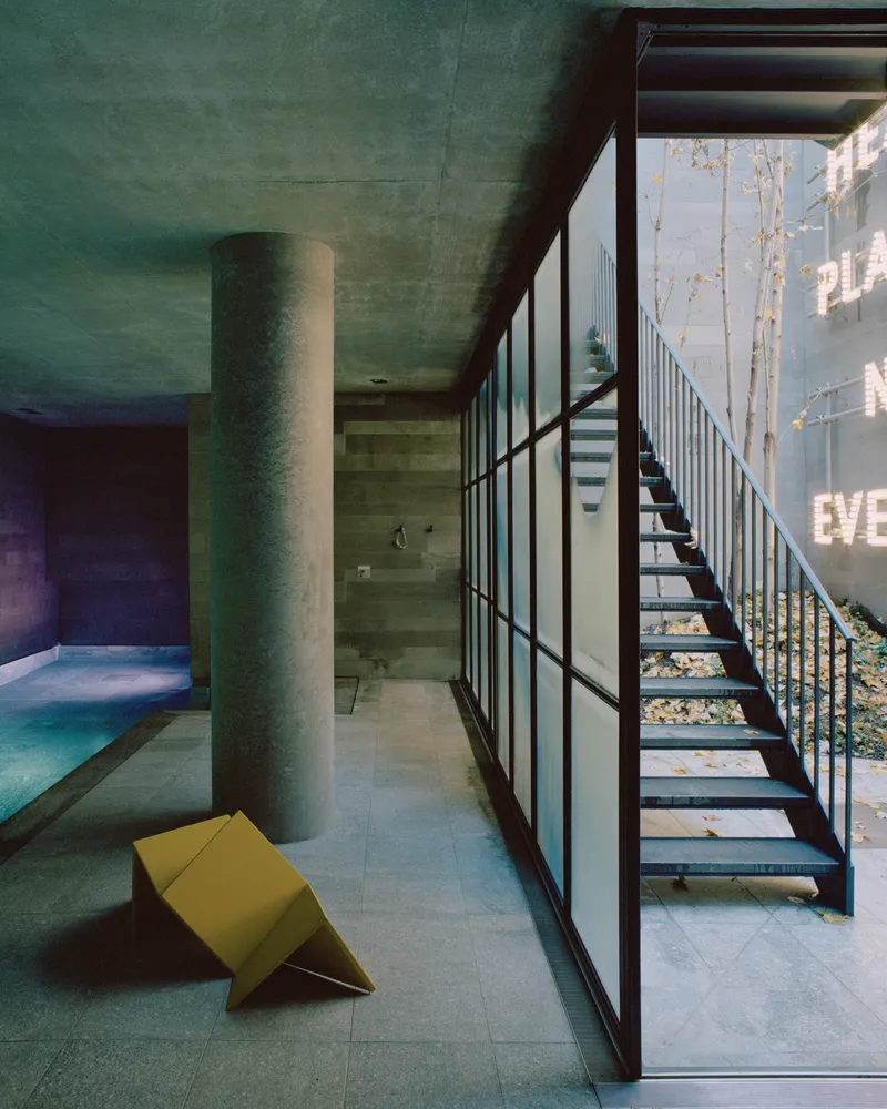 Open steel staircase beside floor-to-ceiling gridded window wall overlooking trees in daylight
