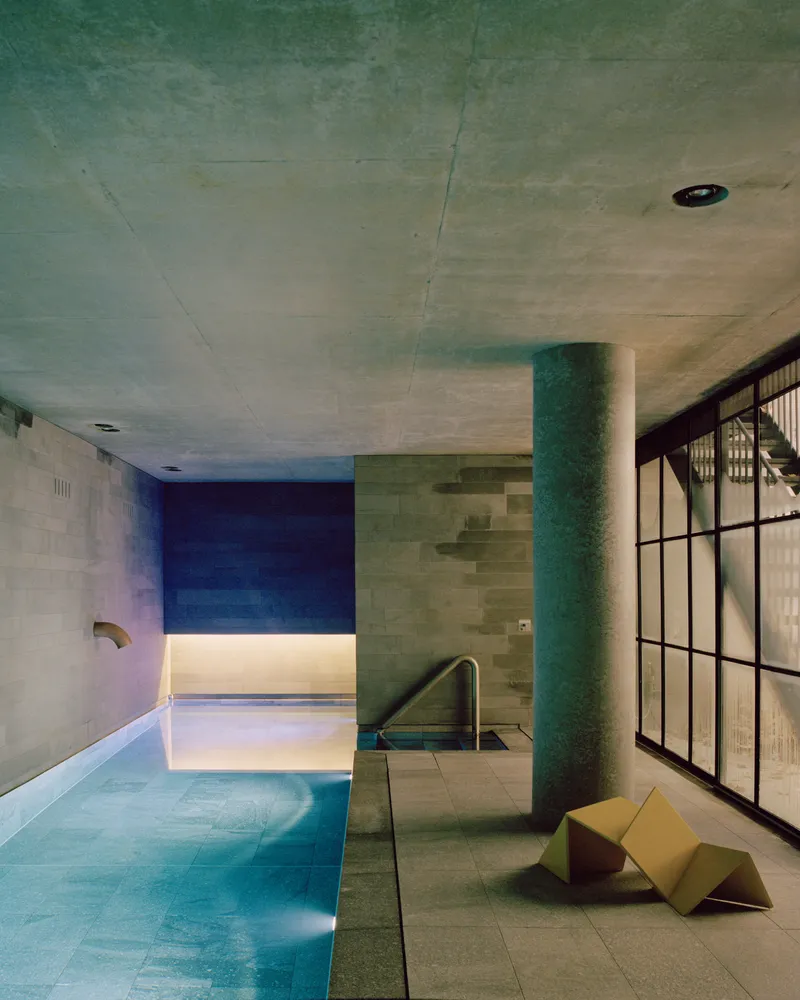 Indoor pool with concrete ceiling and cylindrical green column beside steel-framed glazing