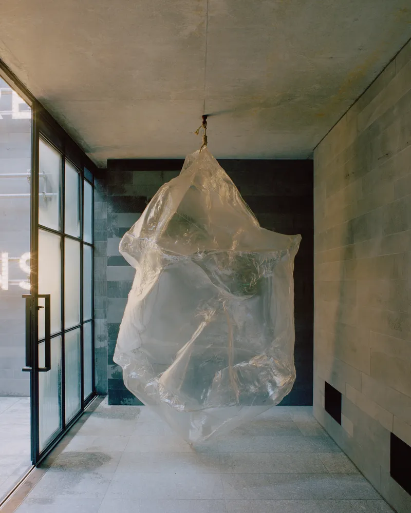 Interior hallway with suspended translucent sculpture beside glazed wall and board-formed concrete surfaces