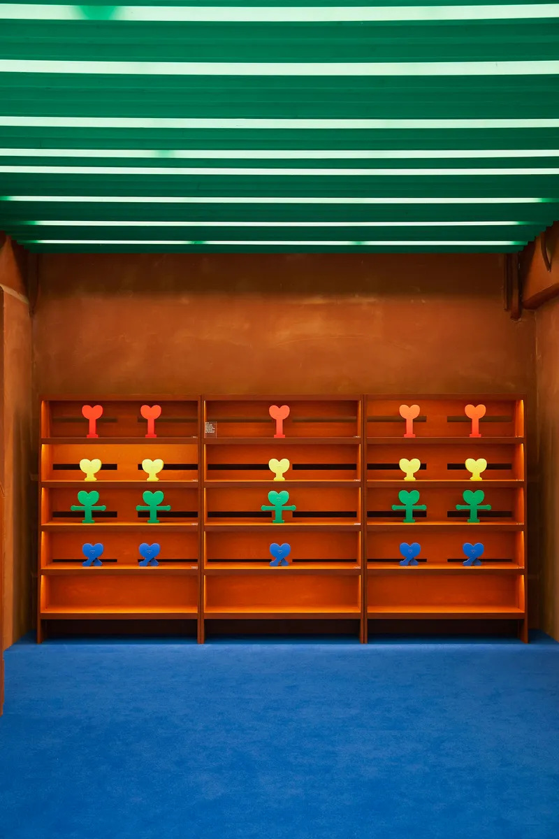Built-in shelving wall displaying colorful sculptural objects in rows beneath green linear ceiling strips