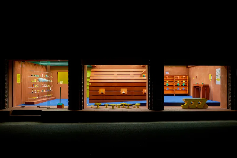 Three storefronts at night revealing interiors with timber furnishings, shelving, and blue flooring
