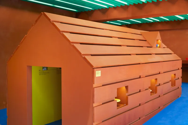 House-shaped installation with layered timber cladding and doorway revealing lime green interior