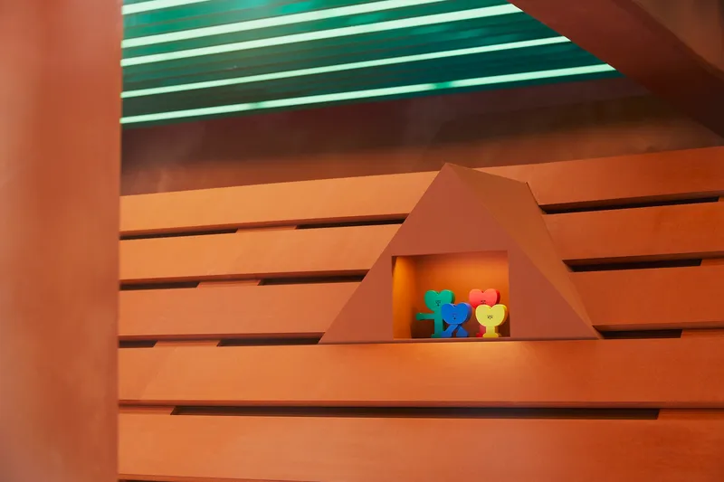 Triangular recess in horizontal wood slat wall with colorful objects under green striped ceiling