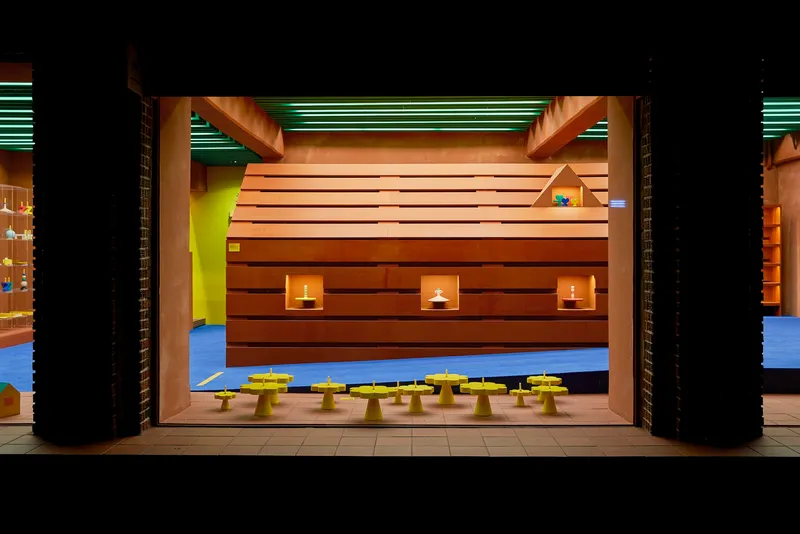 Horizontal wood-clad volume with square window cutouts and candles, flanked by black brick columns at night