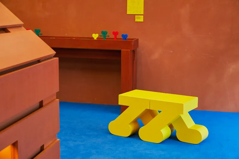Yellow sculptural bench on blue flooring beside terracotta walls and timber built-in furniture