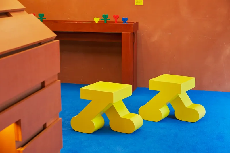 Two yellow stools with curved legs on blue flooring near timber cabinetry and terracotta walls